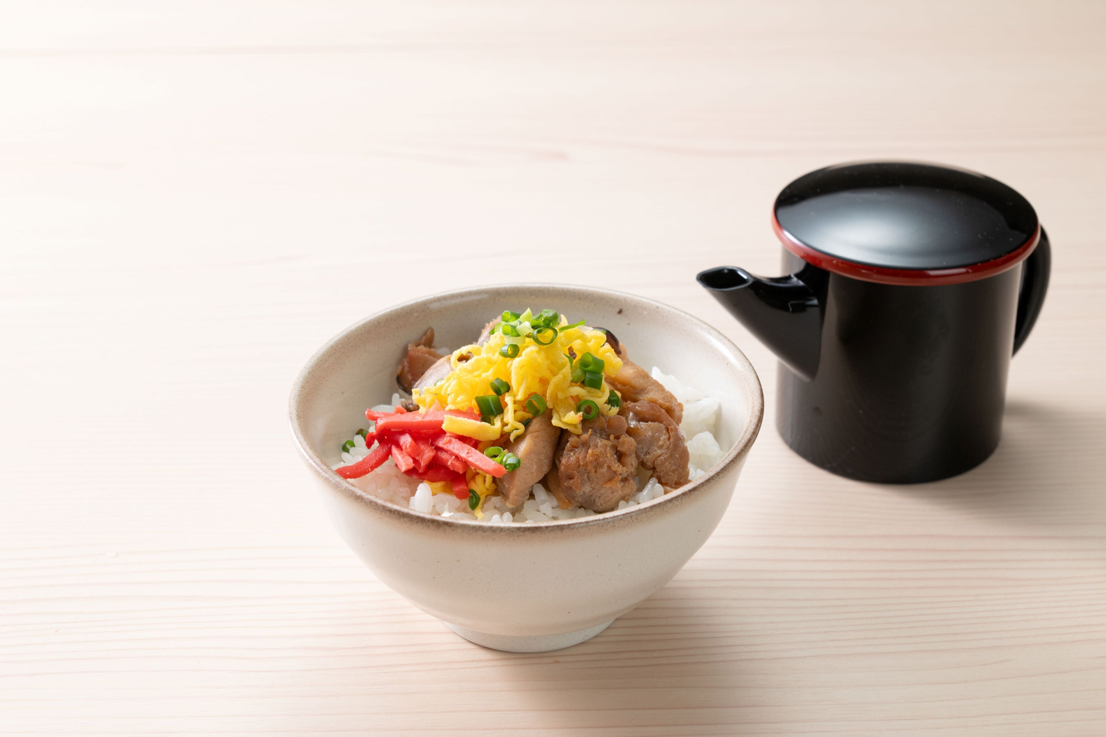A bowl of rice with vegetables and meat, and a black mug on a wooden table.
