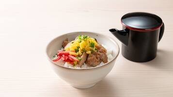 A bowl of rice with vegetables and meat, and a black mug on a wooden table.