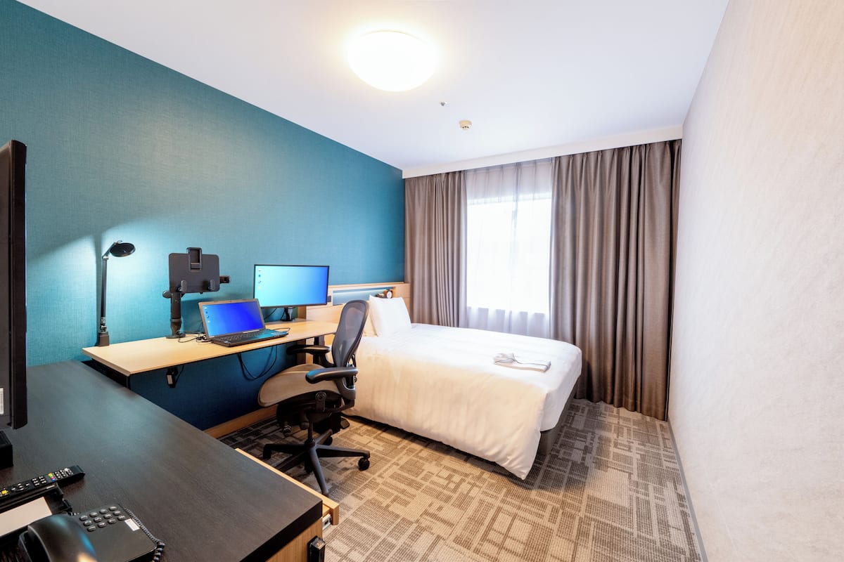 Una habitación de hotel con cama, escritorio, computadora portátil y televisor.