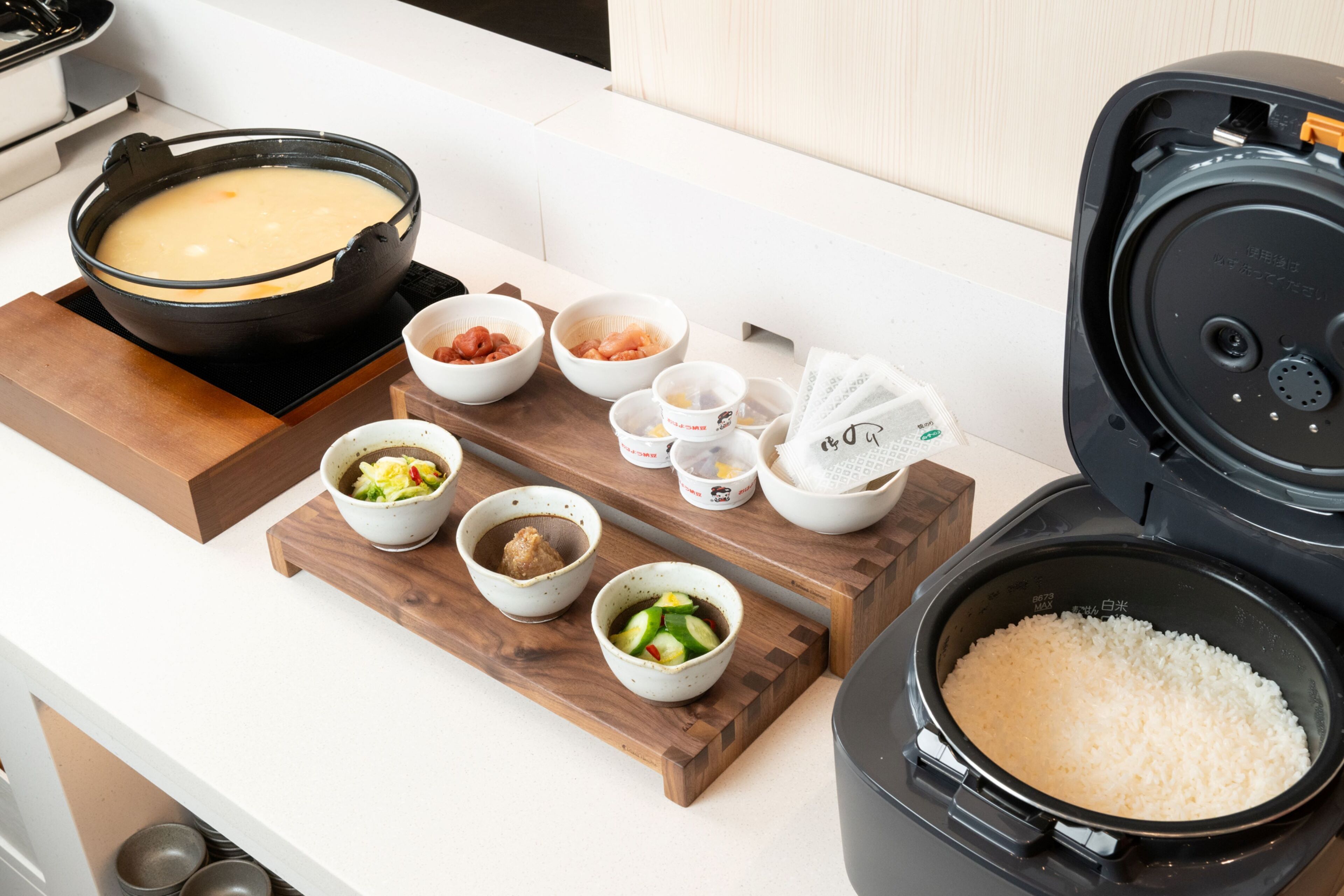 A kitchen counter with various bowls of food, a rice cooker, and a pot of soup.