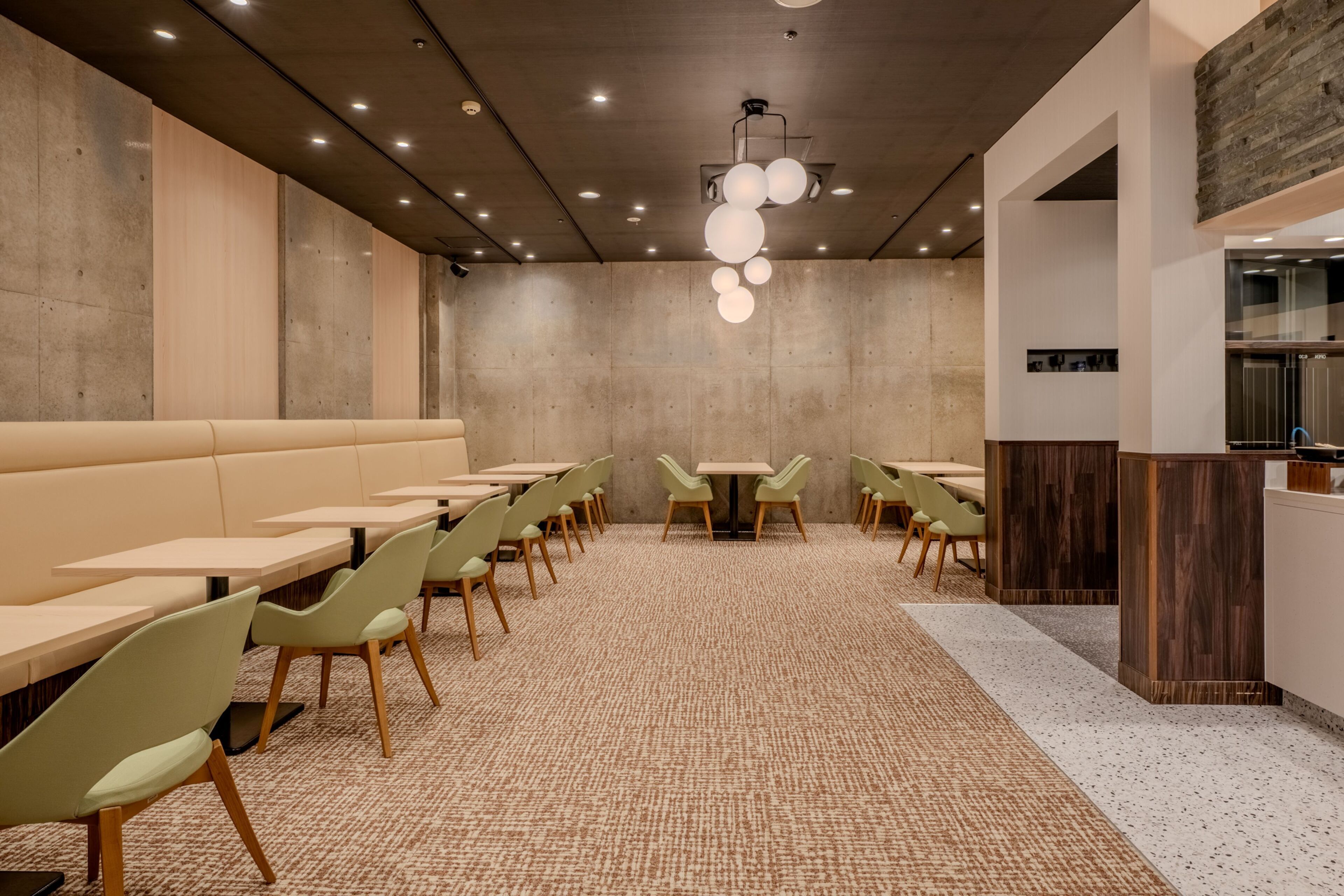 A modern restaurant with a long counter, green chairs, and a patterned carpet.
