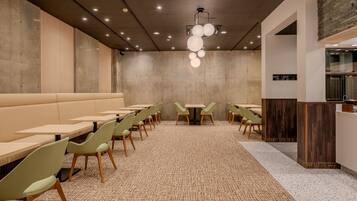 A modern restaurant with a long counter, green chairs, and a patterned carpet.