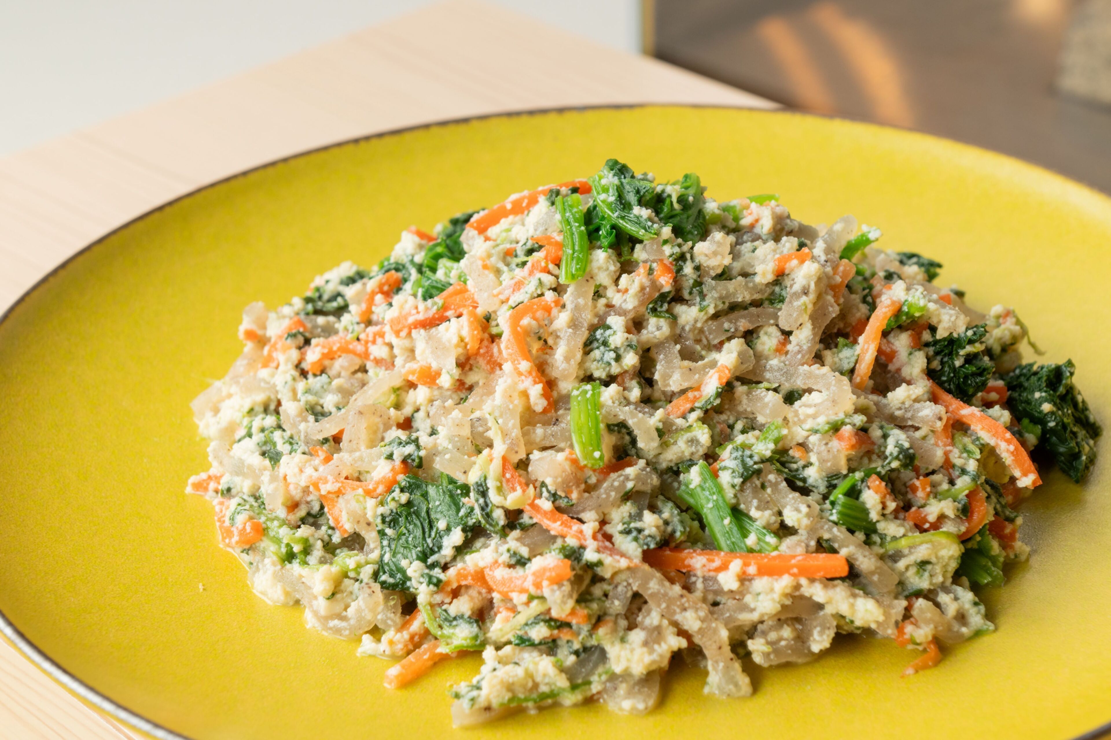 Un plat groc amb un plat de rice, carots i verdura de fulla.