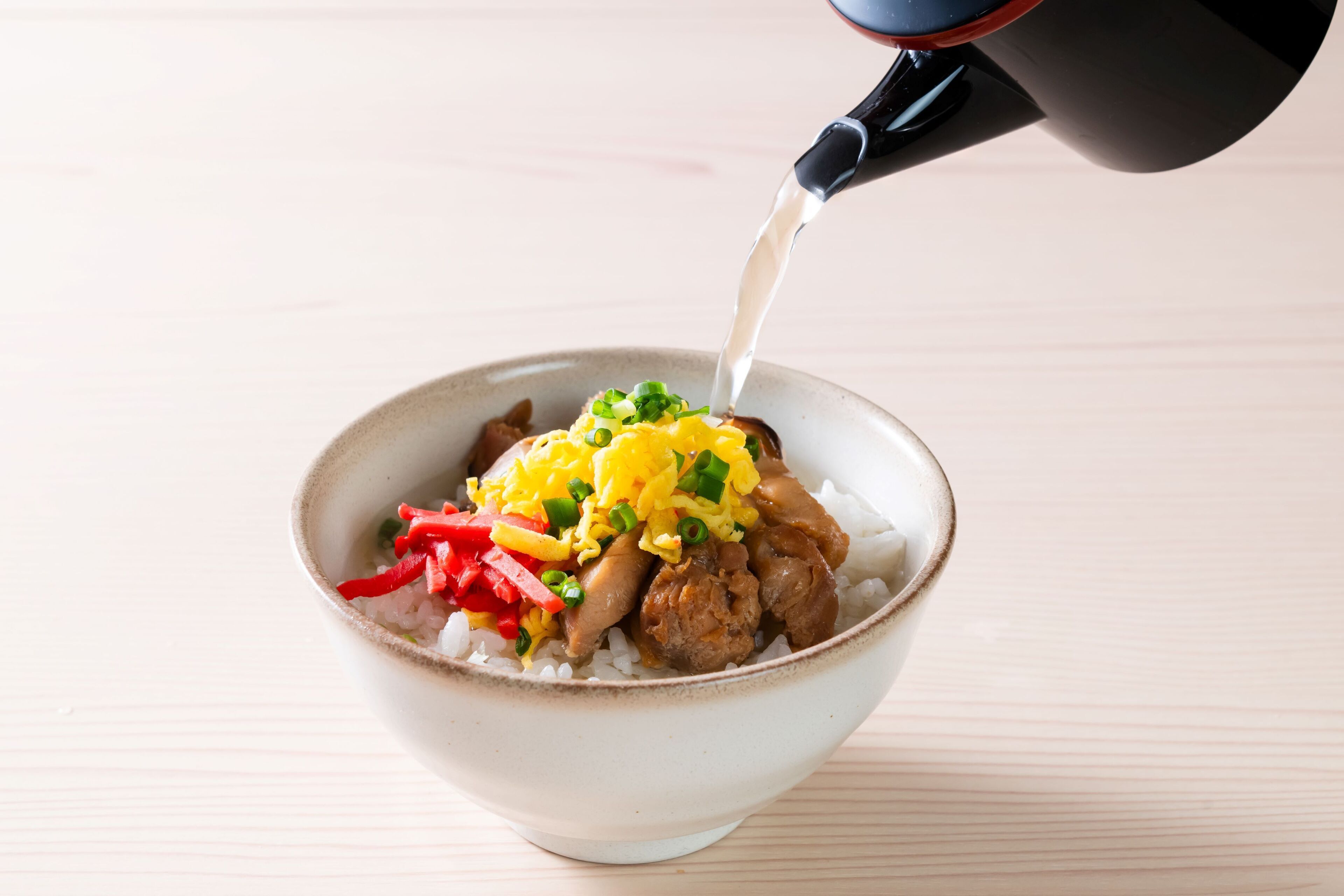 A bowl of rice with meat, vegetables, and a sauce being poured over it.