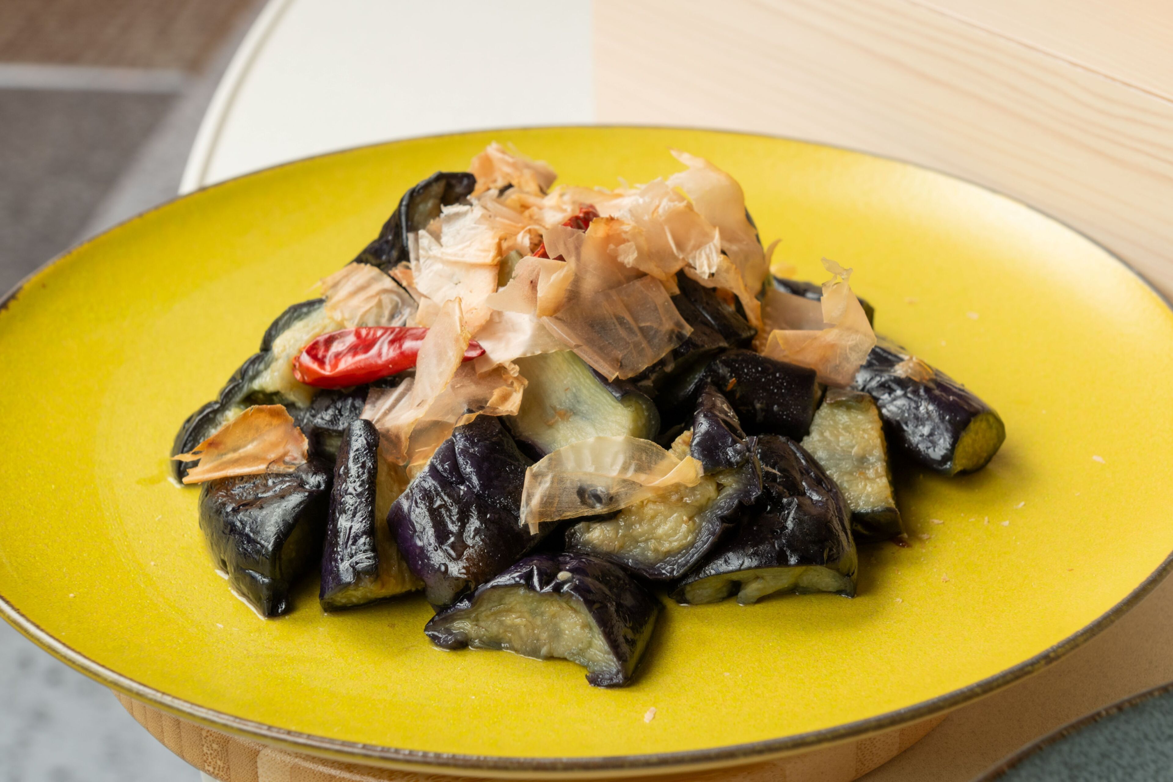 A yellow plate with stuffed eggplants topped with shredded ingredients.