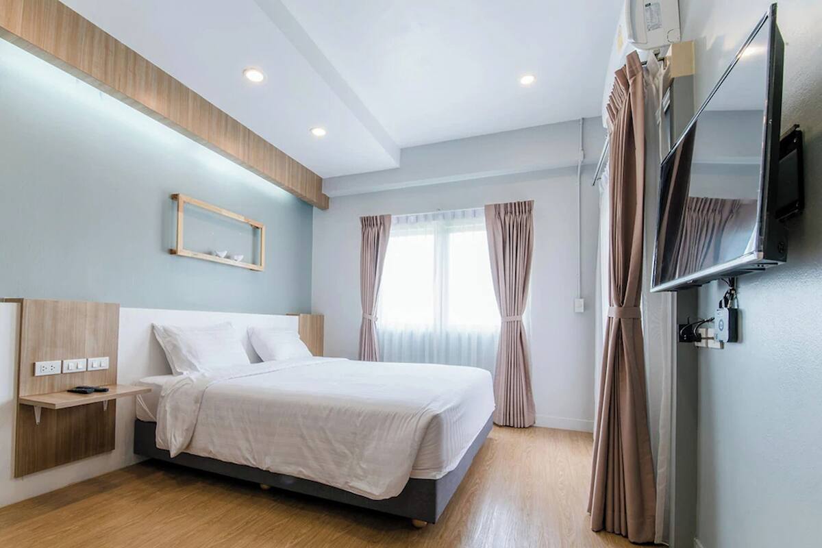 A modern hotel room with a bed, bedside table, TV, and curtains.