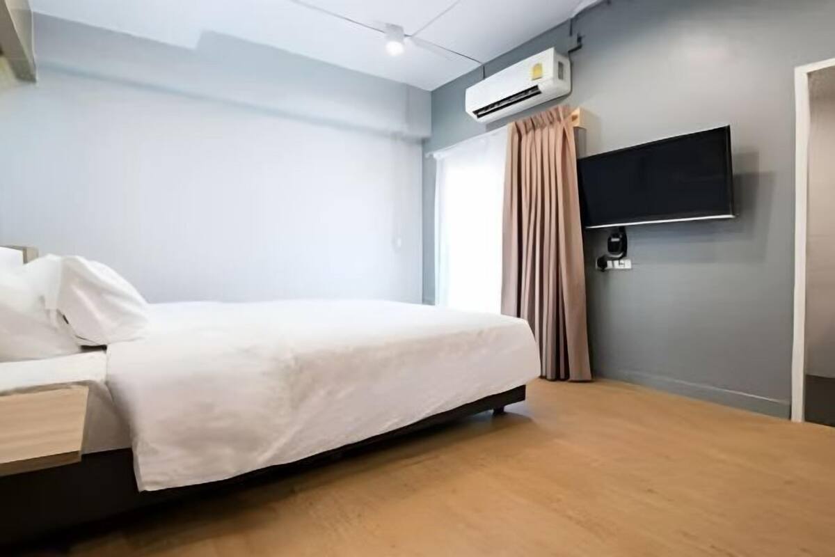 A modern hotel room with a bed, an air conditioning unit, a flat-screen TV, and a wooden floor.