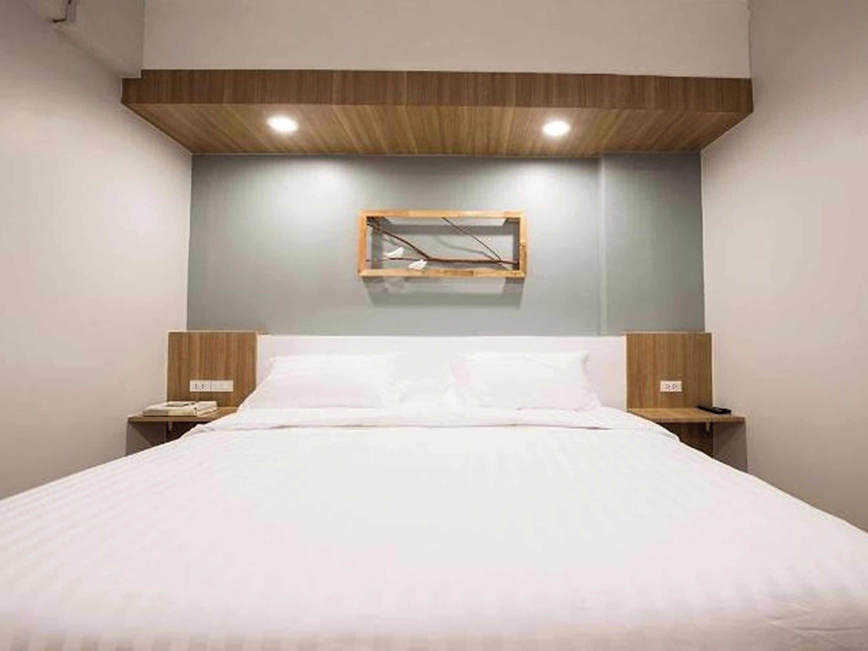 A bedroom with a bed, wooden headboard, bedside tables, and a wall-mounted light fixture.