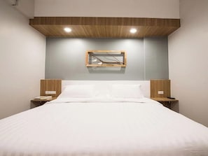 A bedroom with a bed, wooden headboard, bedside tables, and a wall-mounted light fixture.