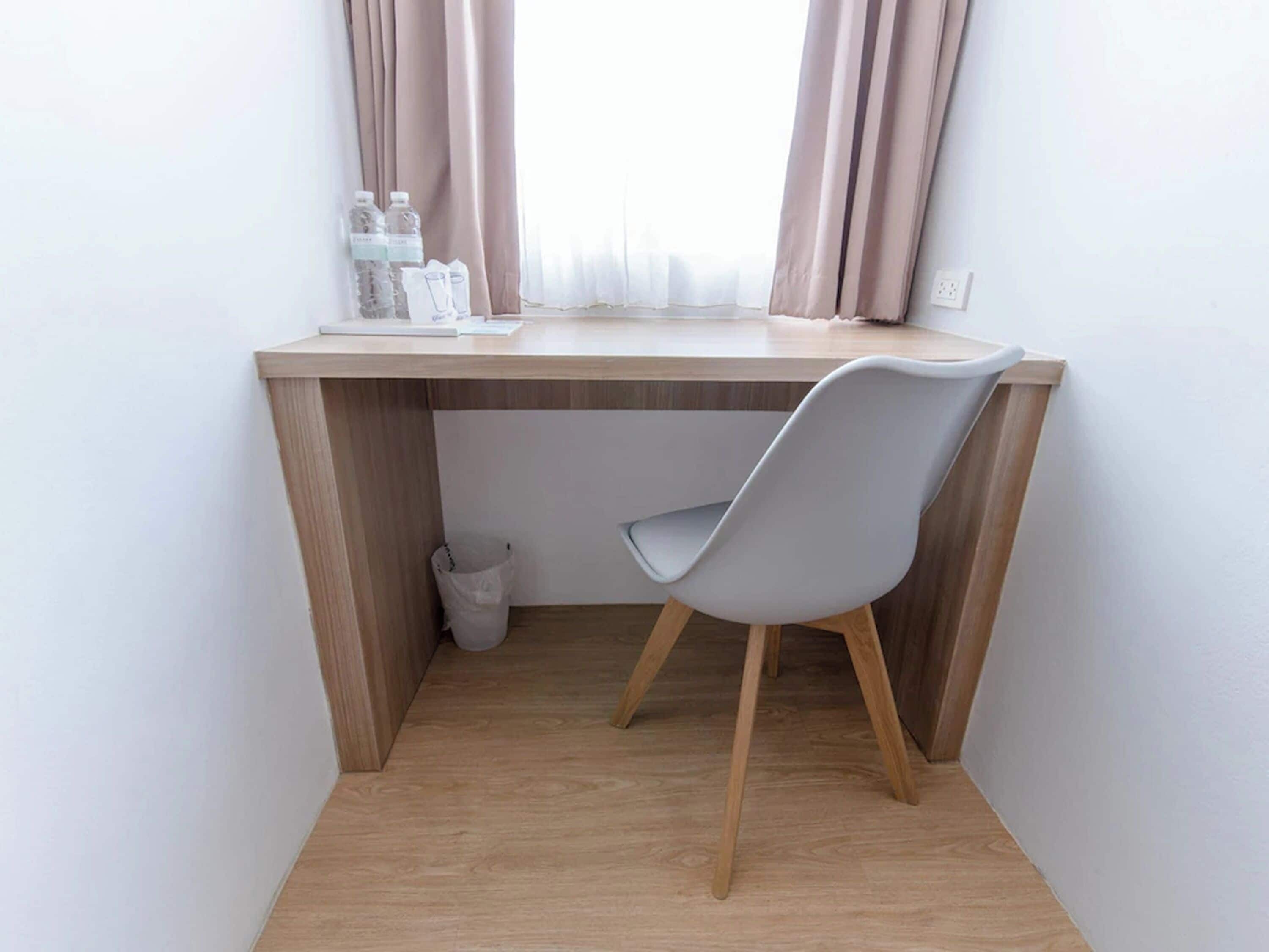 A small, modern workspace with a wooden desk, a grey chair, and a window with curtains.