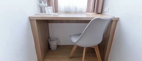 A small, modern workspace with a wooden desk, a grey chair, and a window with curtains.