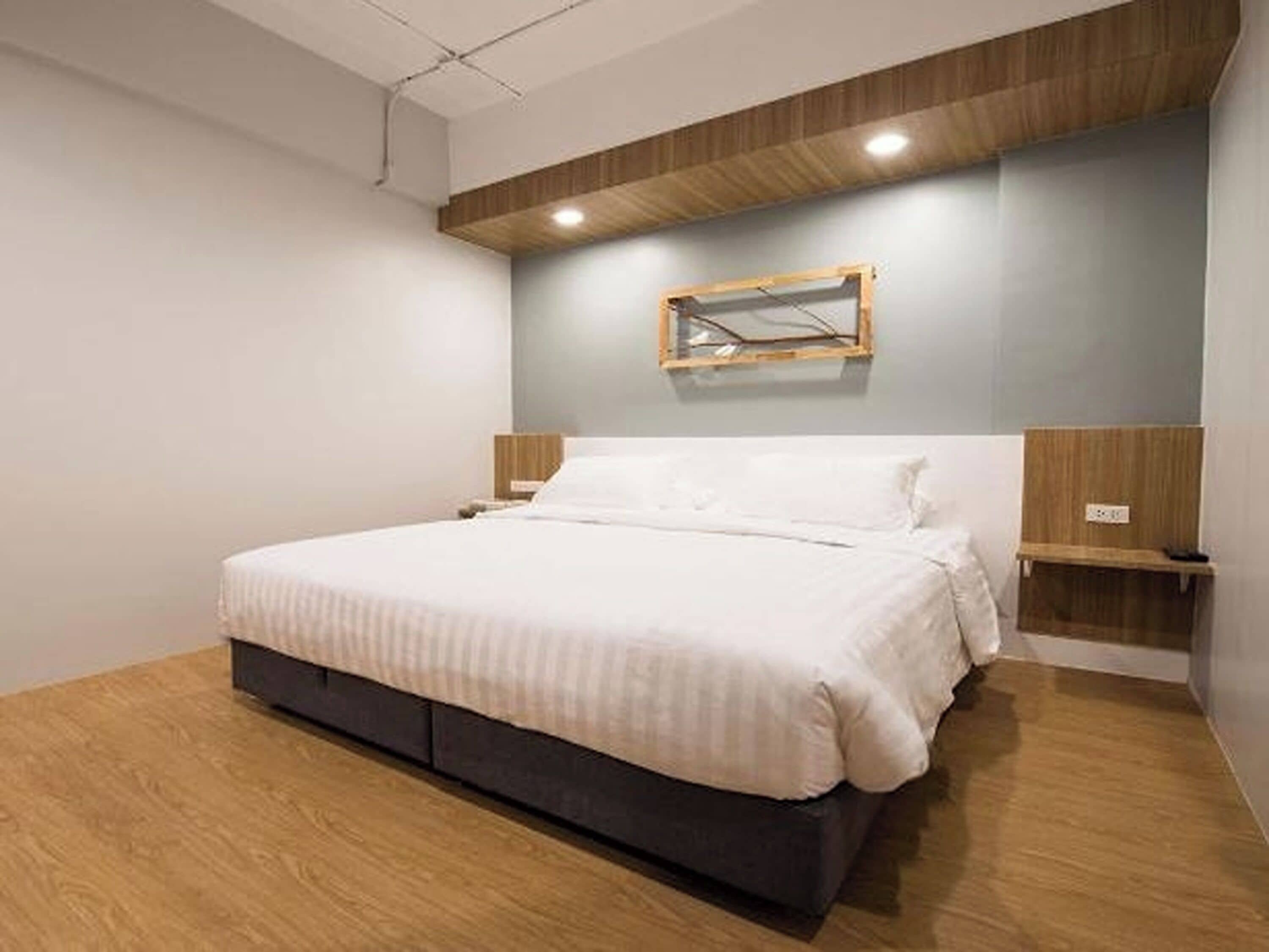 Un dormitorio moderno con cama, cabecera de madera, mesitas de noche y un espejo montado en la pared.