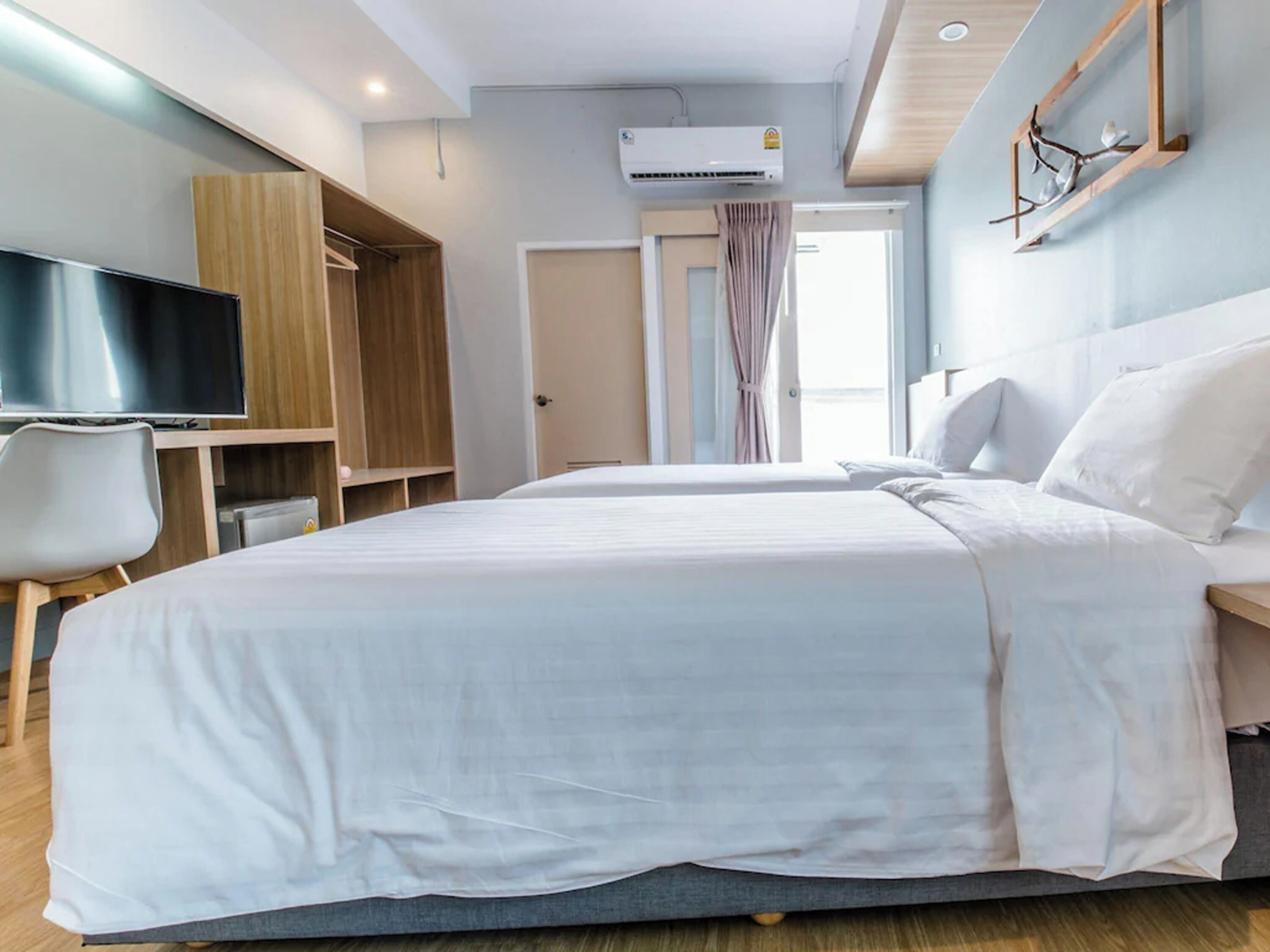 A hotel room with two beds, a TV, a wardrobe, and an air conditioning unit.