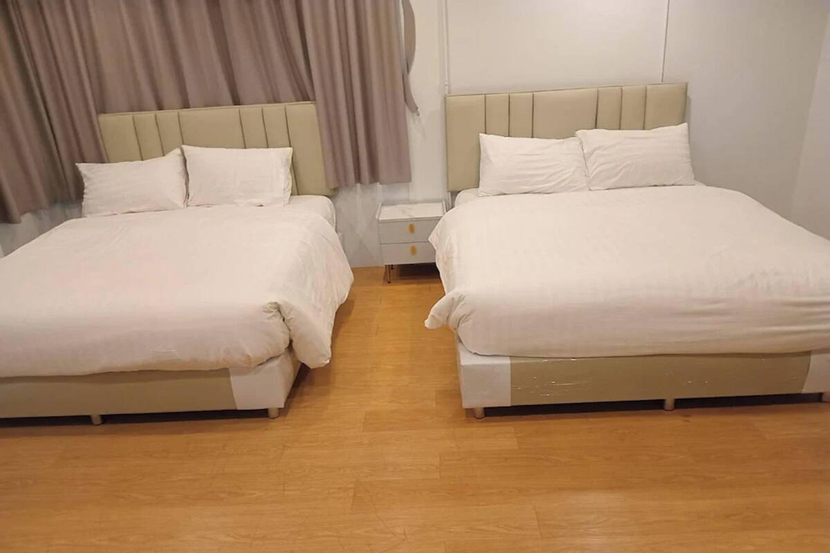 A hotel room with two beds, a nightstand, and a wooden floor.