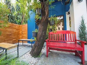 A red bench, a wooden table, and a tree in a courtyard with a blue wall and a wooden fence.