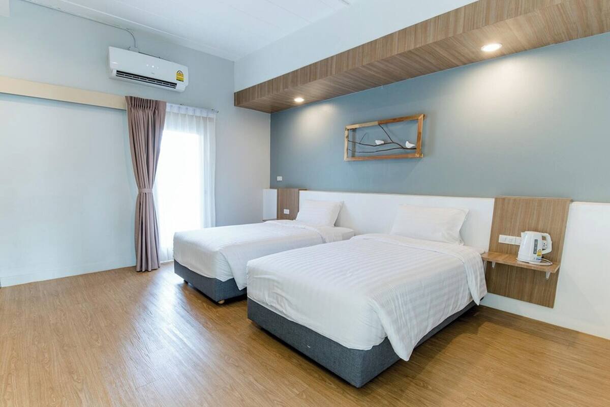 A hotel room with two beds, a wooden ceiling, an air conditioning unit, and a wall-mounted shelf with a kettle.