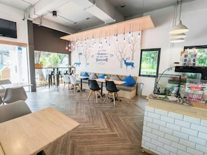 A modern cafe interior with wooden tables and chairs, a wall mural, and a counter with items on display.