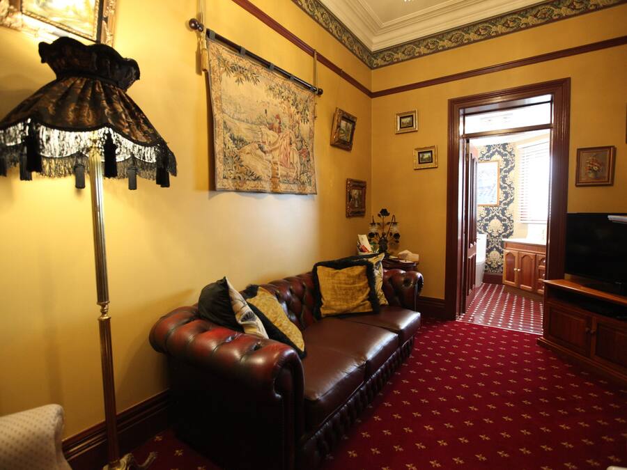 A living room with a red carpet, a dark brown leather sofa, a standing lamp, and a large tapestry on the wall.