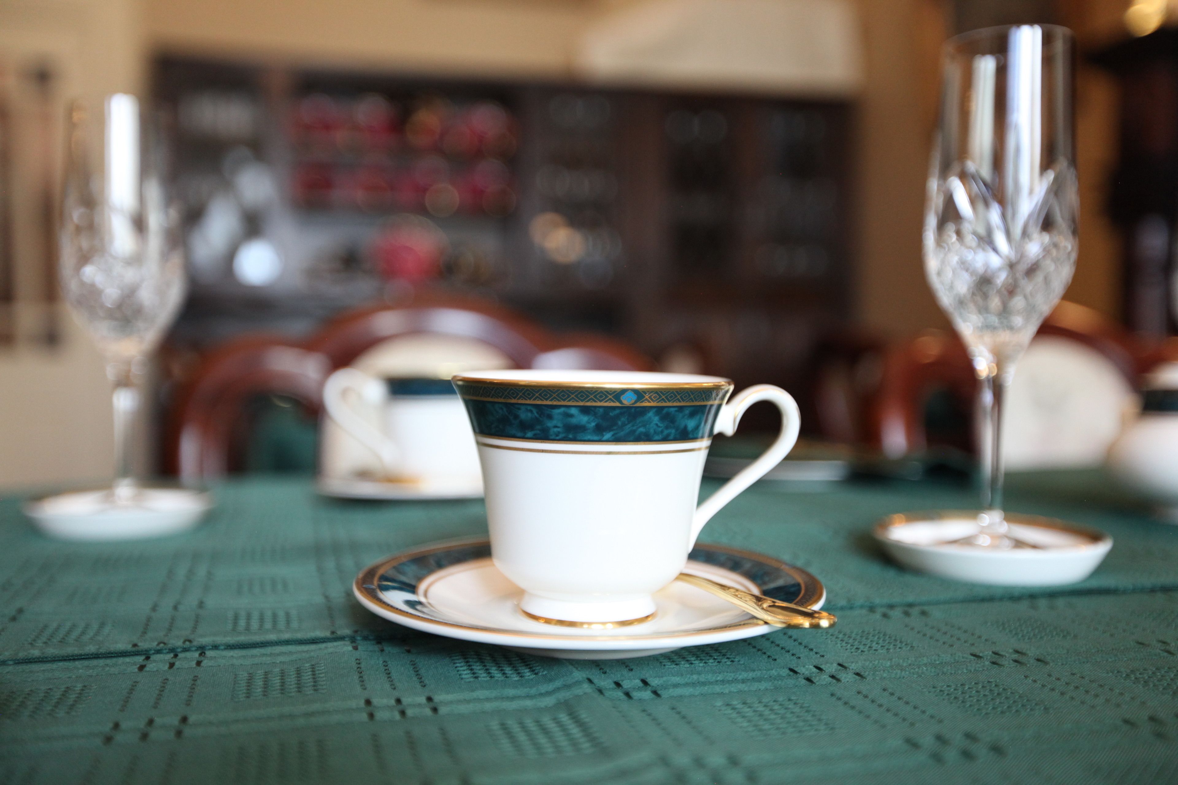 Una mesa con una taza y platillo blancos, una cuchara dorada y dos vasos de cristal.