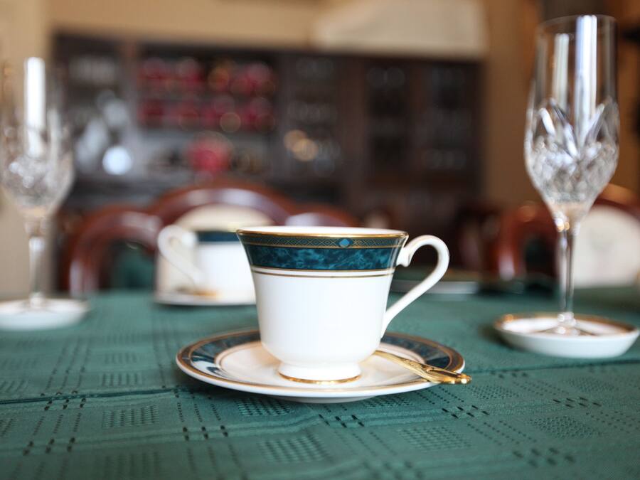 Una mesa con una taza y platillo blancos, una cuchara dorada y dos vasos de cristal.