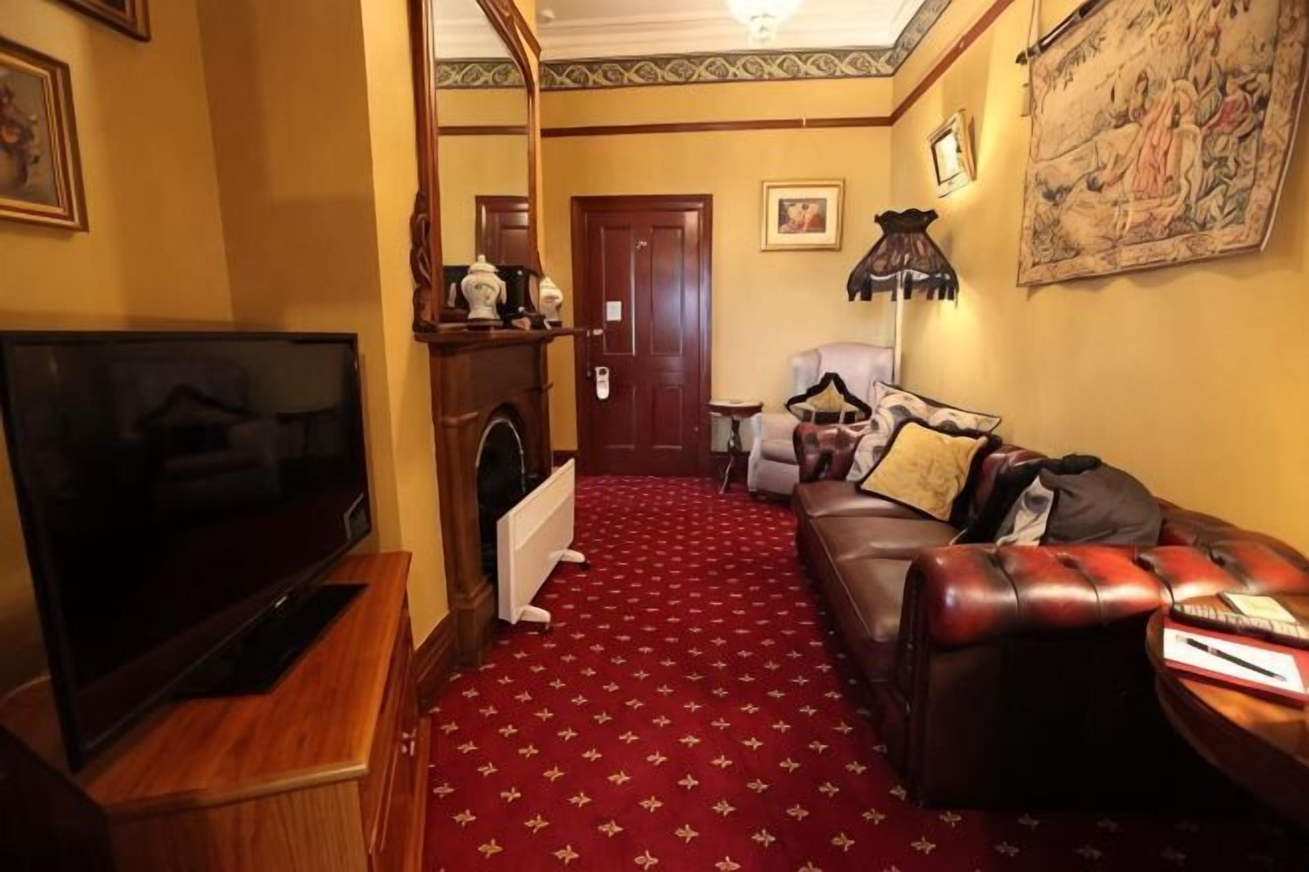 A living room with a television, a fireplace, a red carpet, a leather sofa, and a door leading to another room.