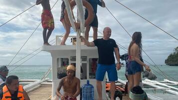 A group of people on a boat with a mast, life preserver, and a water container.