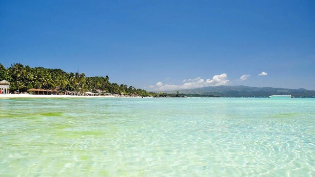 A beach with clear turquoise water, a sandy shore, and a line of palm trees. - Boracay Backpackers (Boracay Island)
