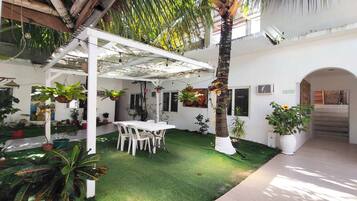 A covered patio area with a white pergola, artificial grass, and potted plants.
