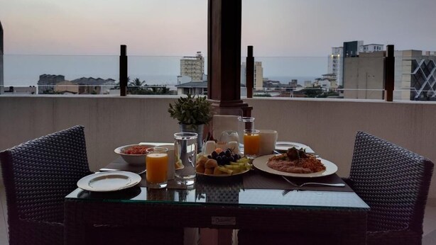 A dining table with breakfast items and a view of the cityscape and ocean. - The Residence (Colombo)