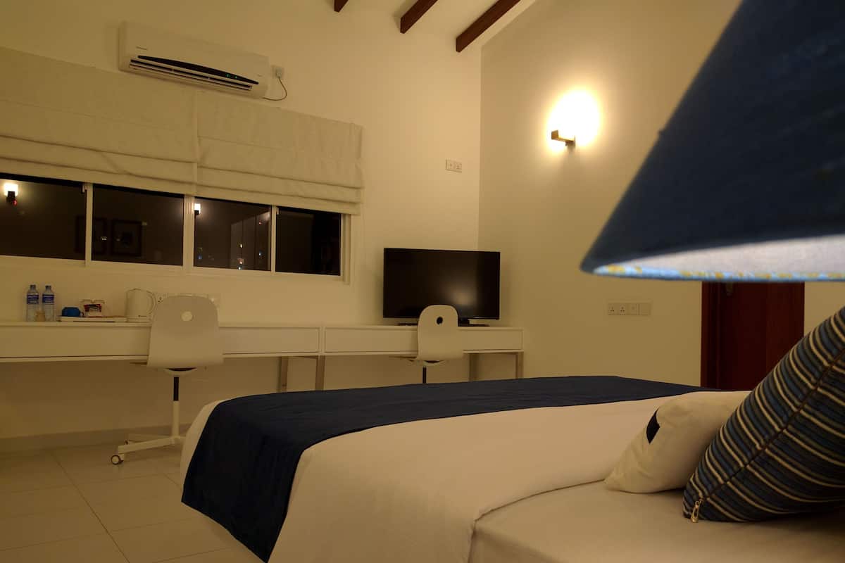A hotel room with a bed, a desk, a chair, a television, and a window.