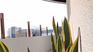 A balcony with large green and yellow plants, a white tiled floor, and a view of buildings in the background. - The Residence (Colombo)