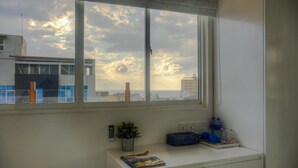 A room with a large window, a desk with a plant, and a view of buildings and clouds. - The Residence (Colombo)