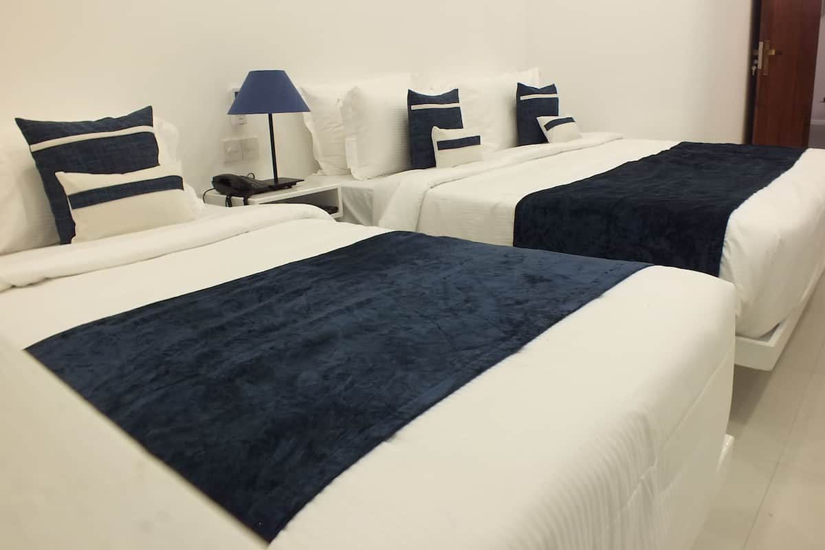 Two beds with white and navy blue bedding, a bedside table with a lamp, and a door in the background.