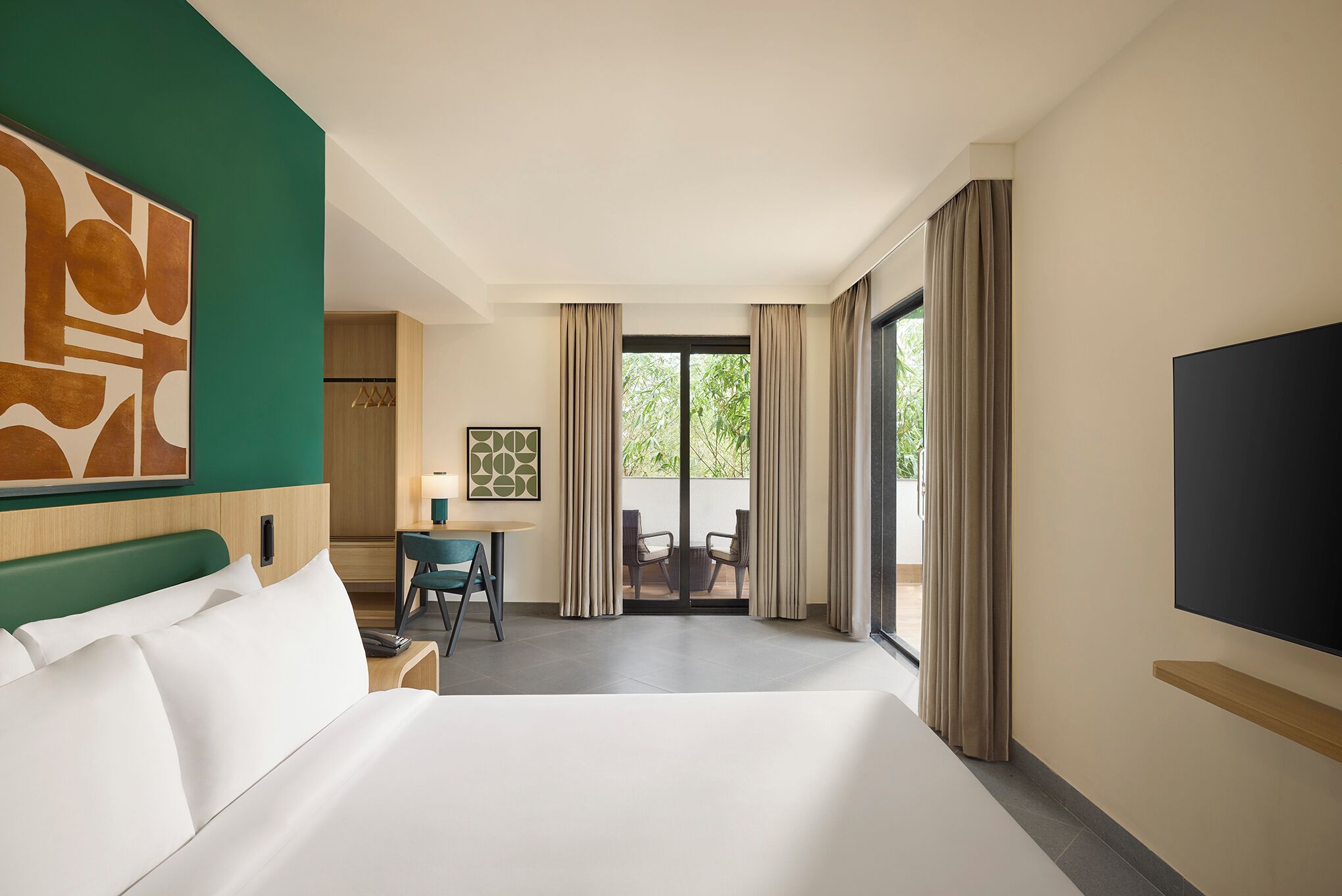 A hotel room with a large bed, a desk, a chair, a TV, and a view of the outdoors.