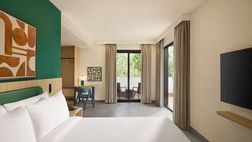 A hotel room with a large bed, a desk, a chair, a TV, and a view of the outdoors.