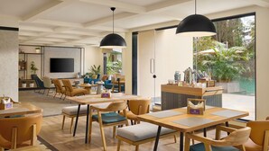 A modern hotel lobby with wooden furniture, black pendant lighting, a reception desk, and a large window with a view of greenery. - Spark by Hilton Goa Calangute (Calangute)