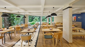 A spacious indoor dining area with multiple tables and chairs, large windows with a view of greenery, and pendant lighting. - Spark by Hilton Goa Calangute (Calangute)