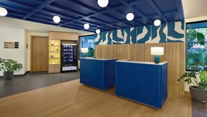 A reception area with a blue reception desk, a wooden wall, a vending machine, and a potted plant. - Spark by Hilton Goa Calangute (Calangute)