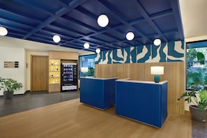 Un espace d’accueil avec un comptoir de réception bleu, un mur en bois, un distributeur automatique et une plante en pot.