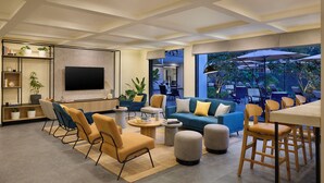A modern living room with a flat-screen TV, comfortable seating, a coffee table, and a large window overlooking an outdoor area with umbrellas. - Spark by Hilton Goa Calangute (Calangute)