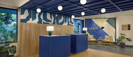A reception desk with a blue and white patterned wall, a wooden panel wall, and a ceiling with blue beams and round lights.