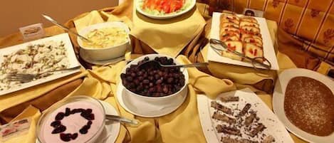 A table with various dishes including a cake, a bowl of cherries, and a plate of sliced meat.