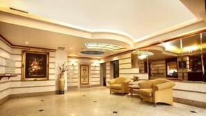 A spacious lobby with a high ceiling, a central seating area with armchairs, a large painting on the wall, and a decorative vase. - Capri Hotel Suites (Amman)