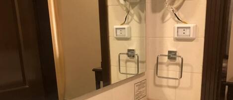 Uma casa de banho com uma pia, um espelho e dois secadores de cabelo fixados na parede.