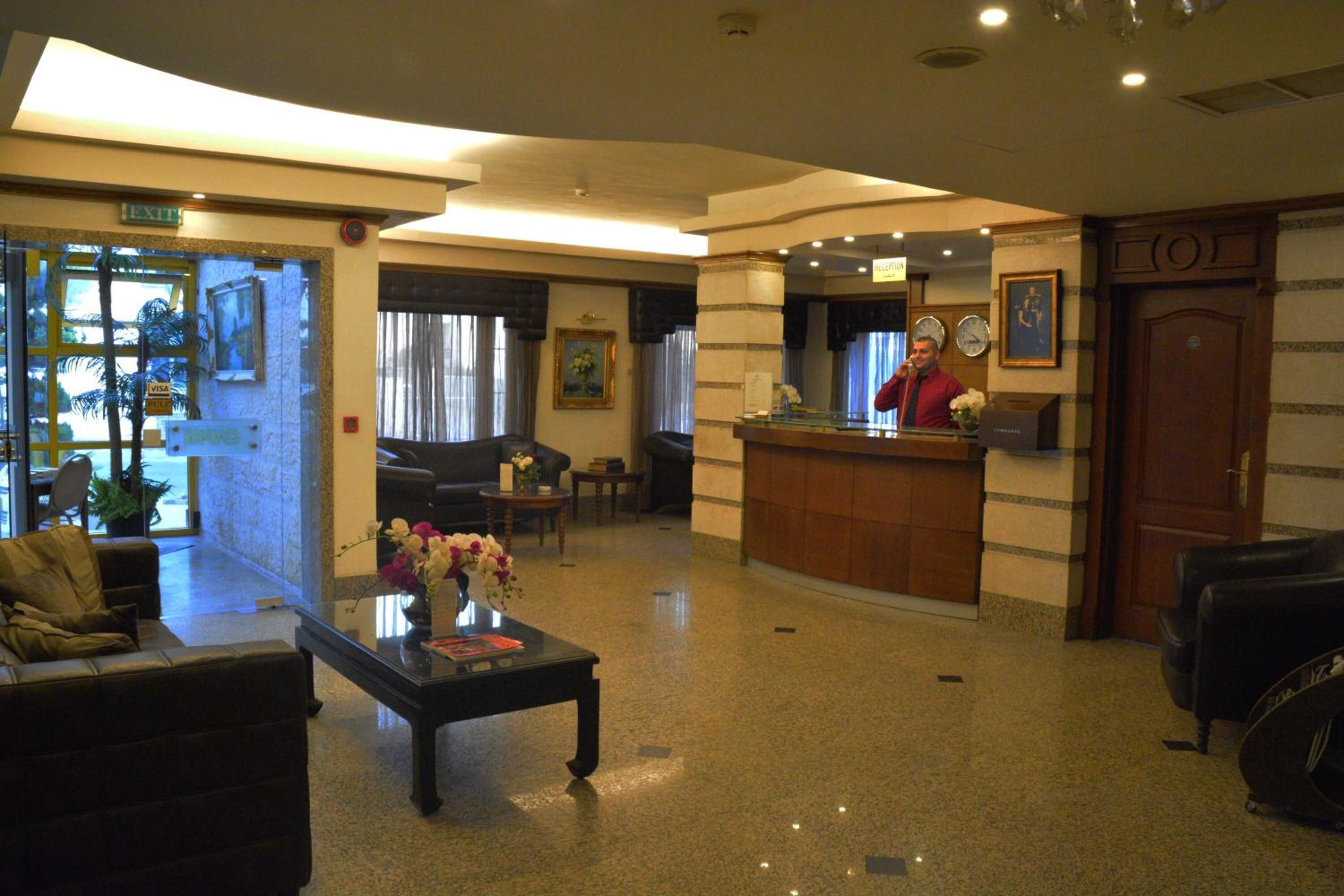 A hotel lobby with a reception desk, seating area, and a coffee table with flowers.