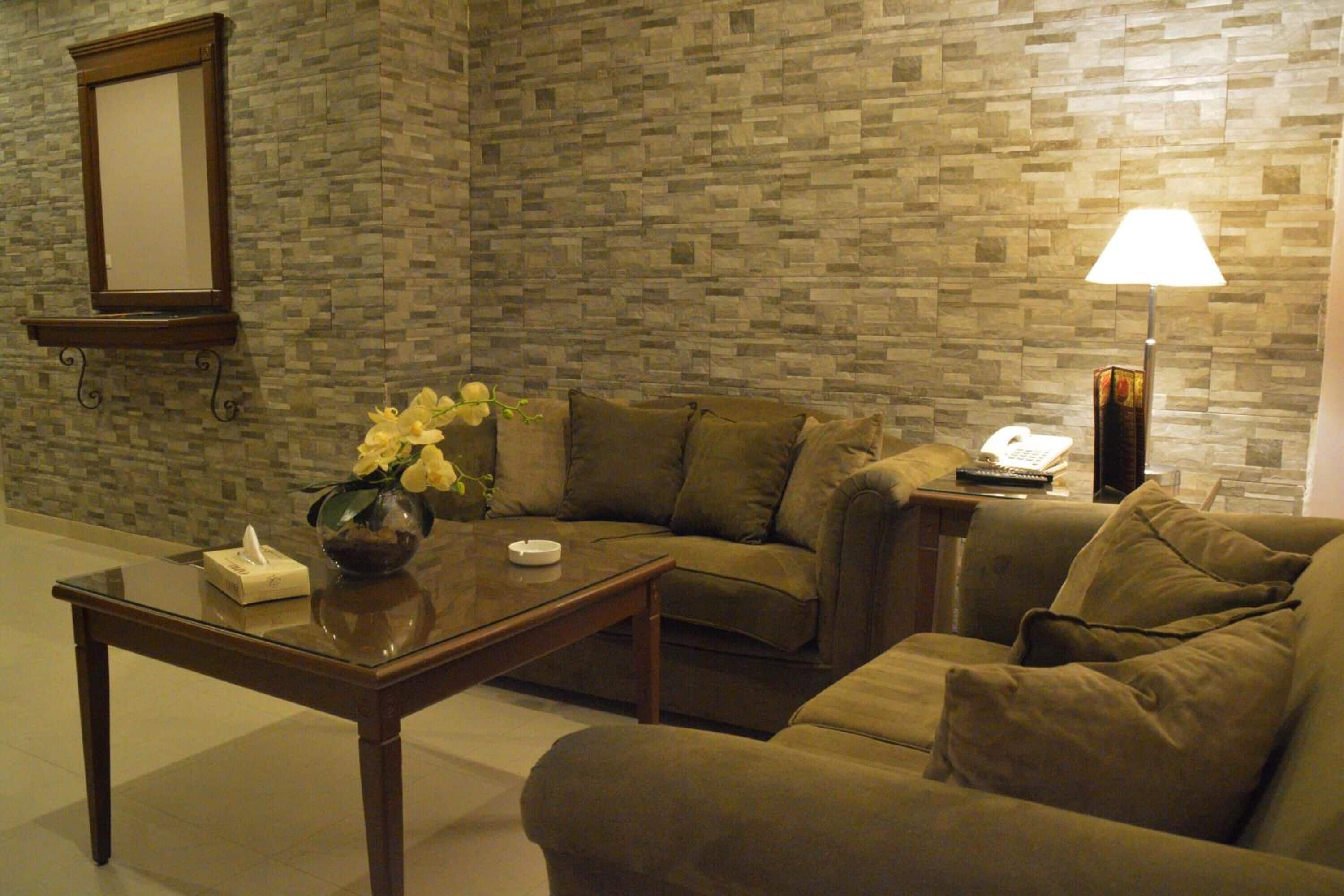 A living room with a brown sofa, a glass coffee table, a vase with flowers, a lamp, and a telephone.