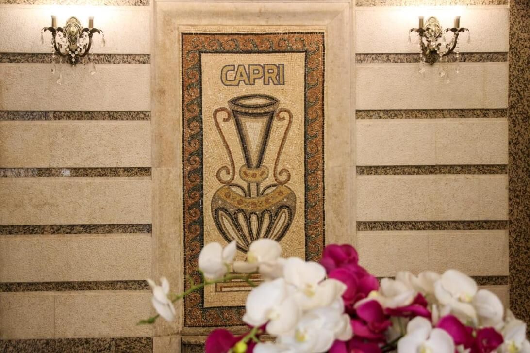 A framed artwork with the word "CAPRI" and a trophy design, flanked by wall sconces.
