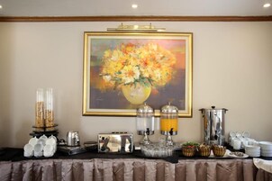 Montaje de un bufé de desayuno con un cuadro de flores en la pared, una máquina de café y distintos dispensadores de comida y bebida.