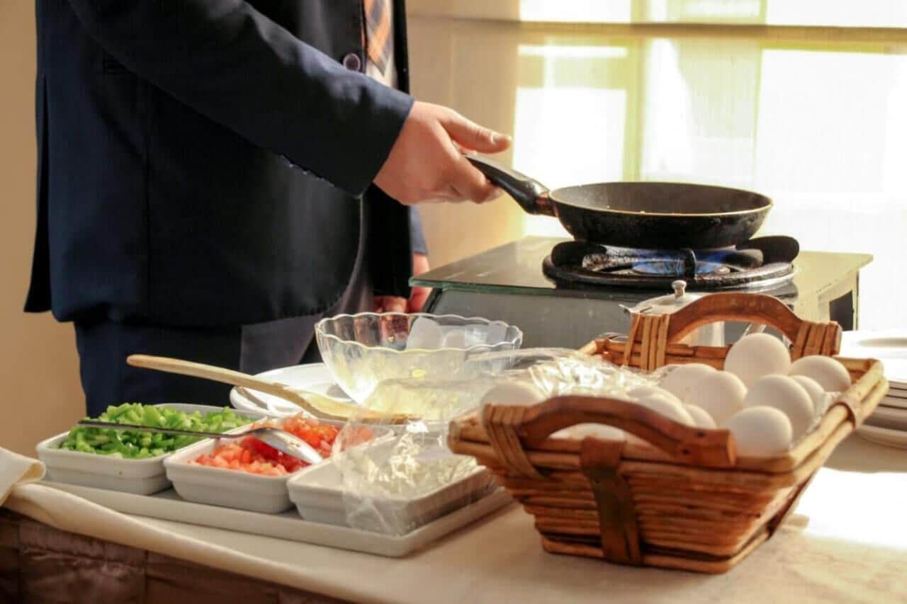 A person cooking with a frying pan on a stove, surrounded by various food items and utensils.