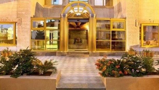 A hotel entrance with a grand archway, large windows, and a checkered pavement leading up to it. - Capri Hotel Suites (Amman)